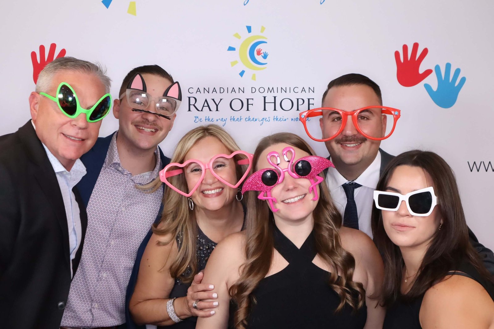 Guests at a Ray of Hope corporate event posing with fun props in a photo booth